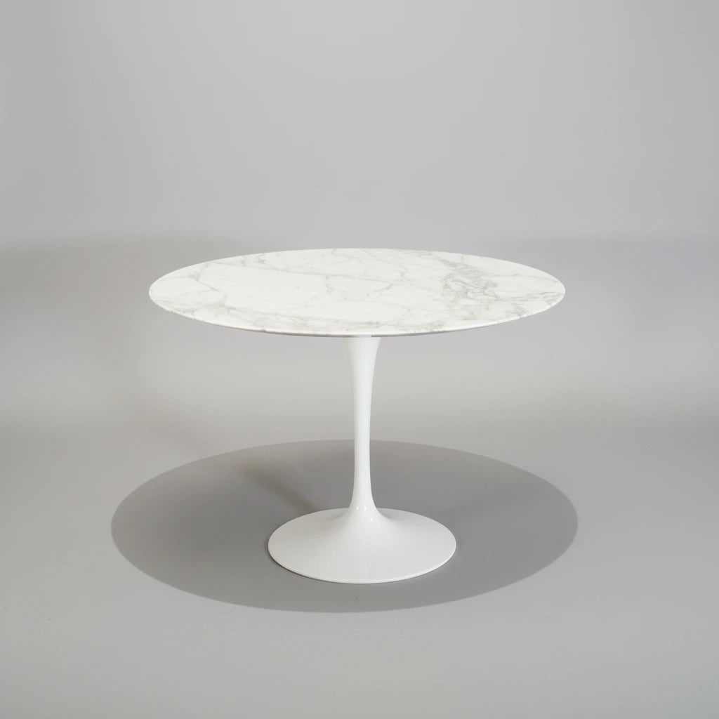A round white marble-top pedestal dining table with a white tulip base, set against a dark gray studio background.
