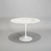 A round white marble-top pedestal dining table with a white tulip base, set against a dark gray studio background.